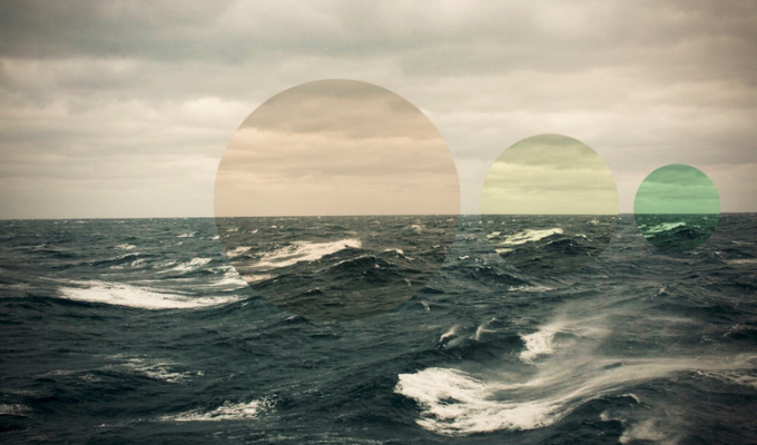 A choppy ocean and cloudy skies with a design of three coloured circles over it. The transparent circles are coloured orange, yellow and green and get consecutively smaller.